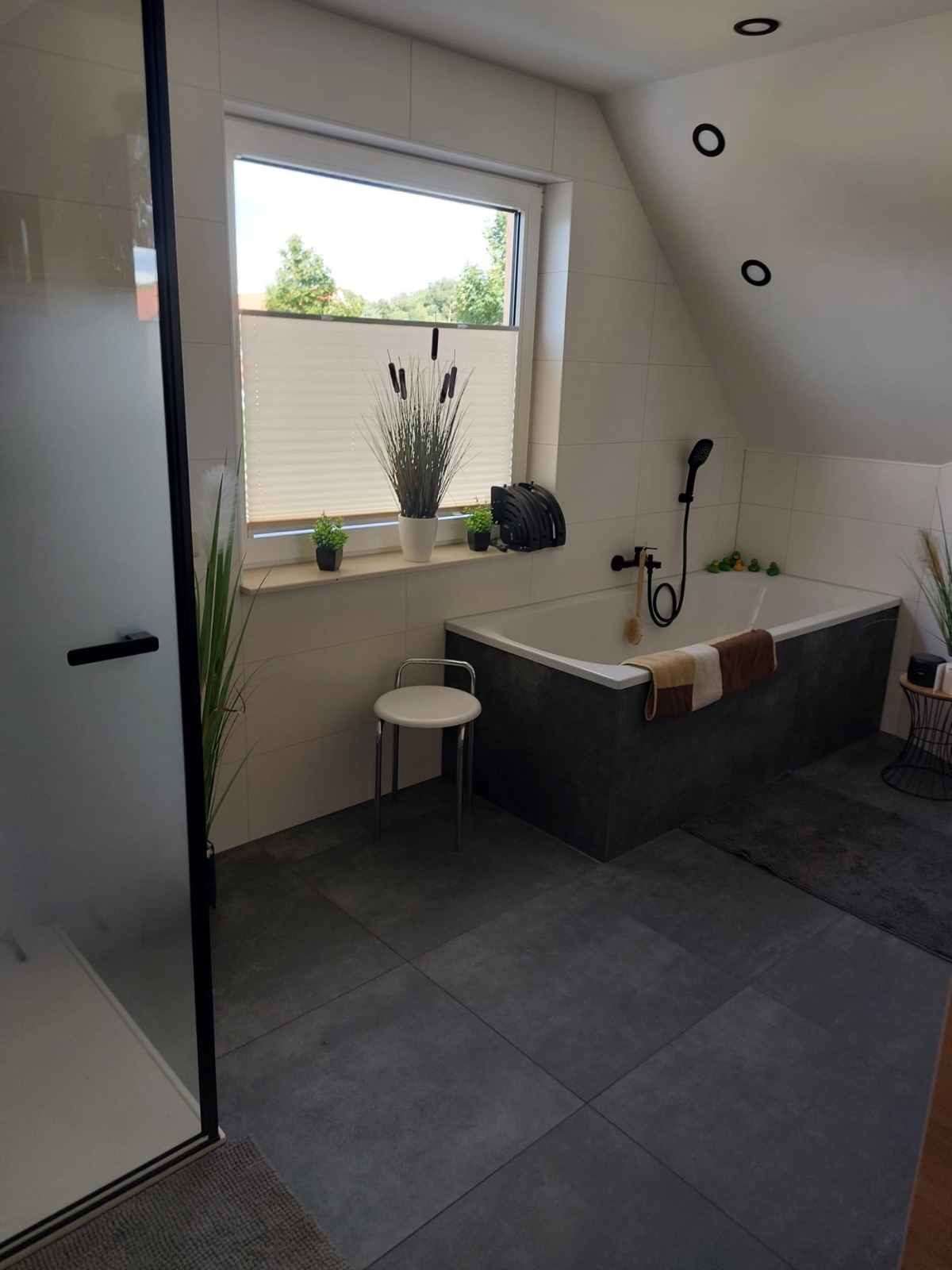 Fertig saniertes Badezimmer mit Badewanne, anthrazitfarbenen Fliesen und Dachschräge