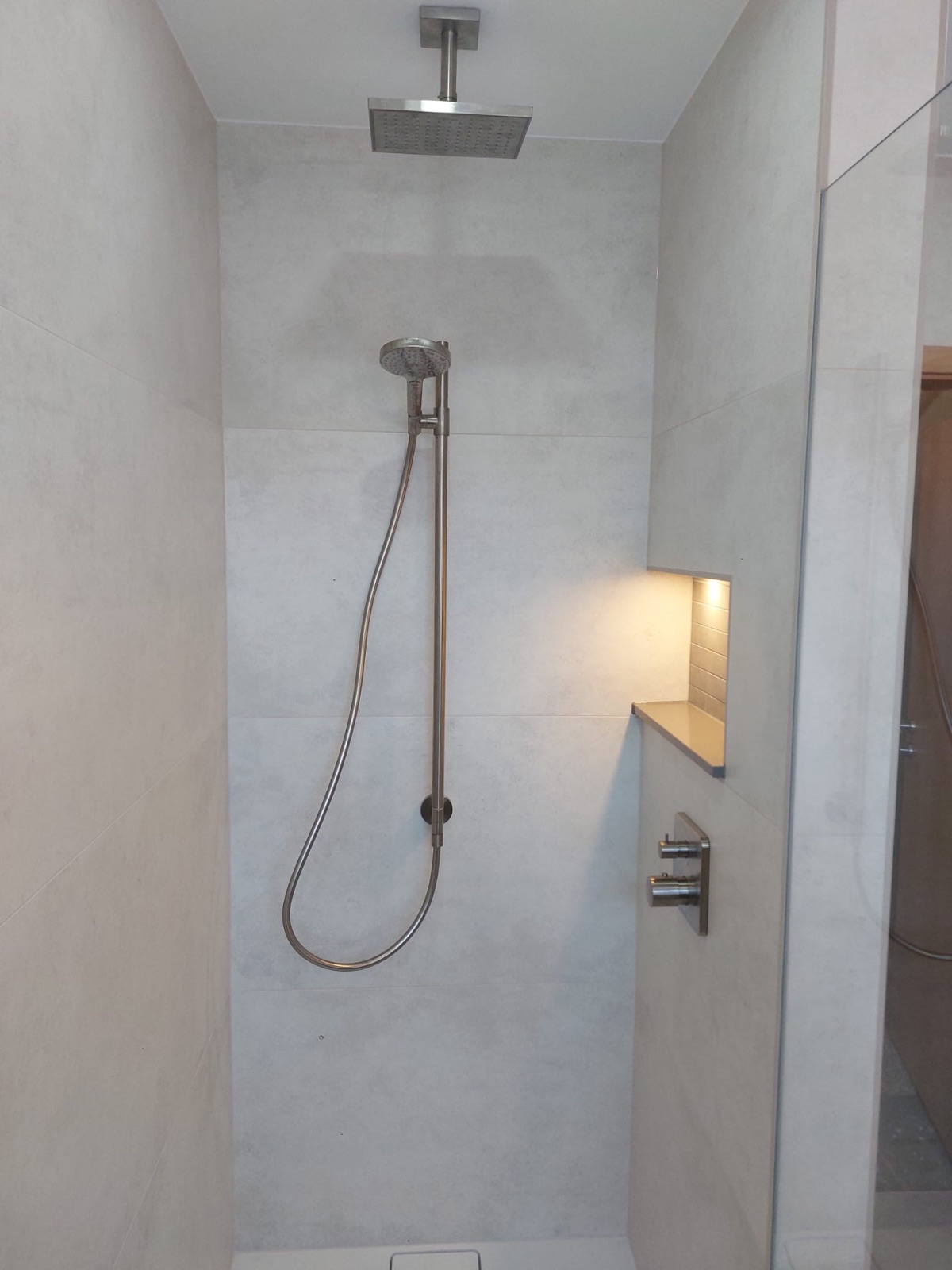 Dusche mit Regenbrause und gefliester Ablagenische