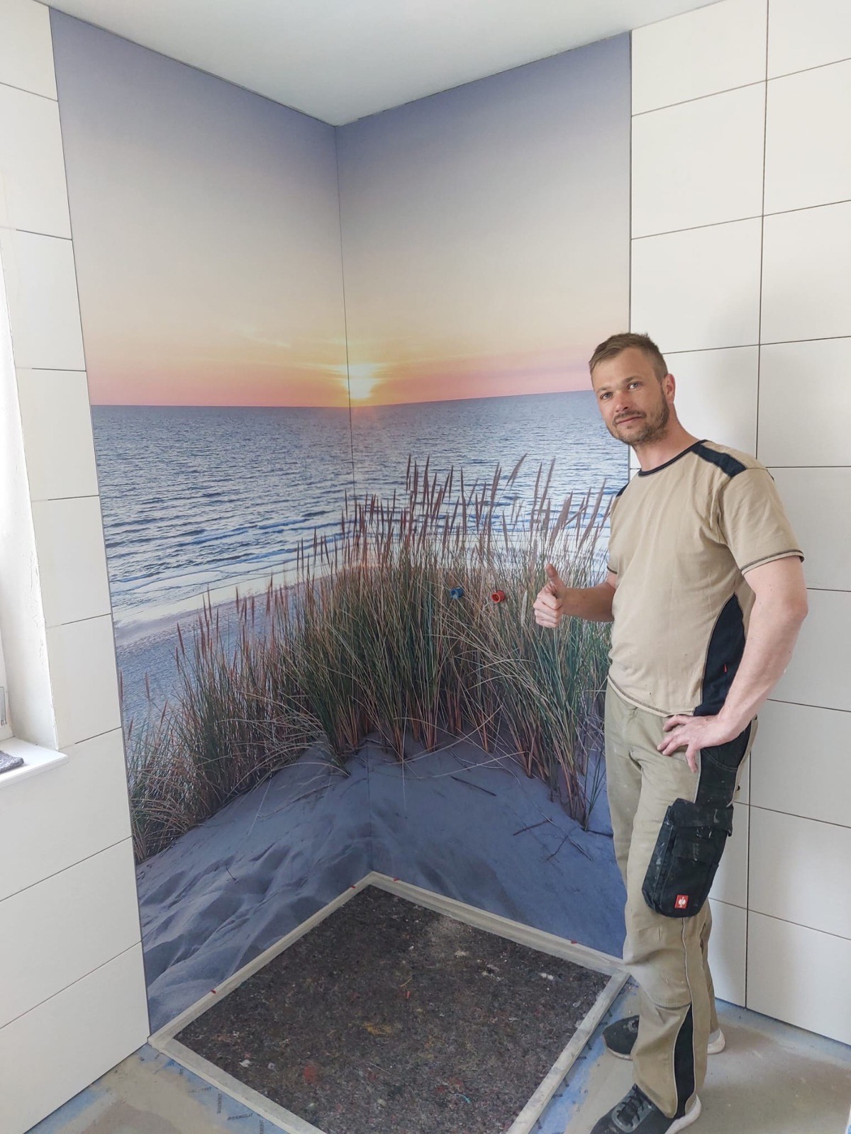 Reimund Jakob bei der Arbeit an einer gefliesten Duschwand mit Strandmotiv